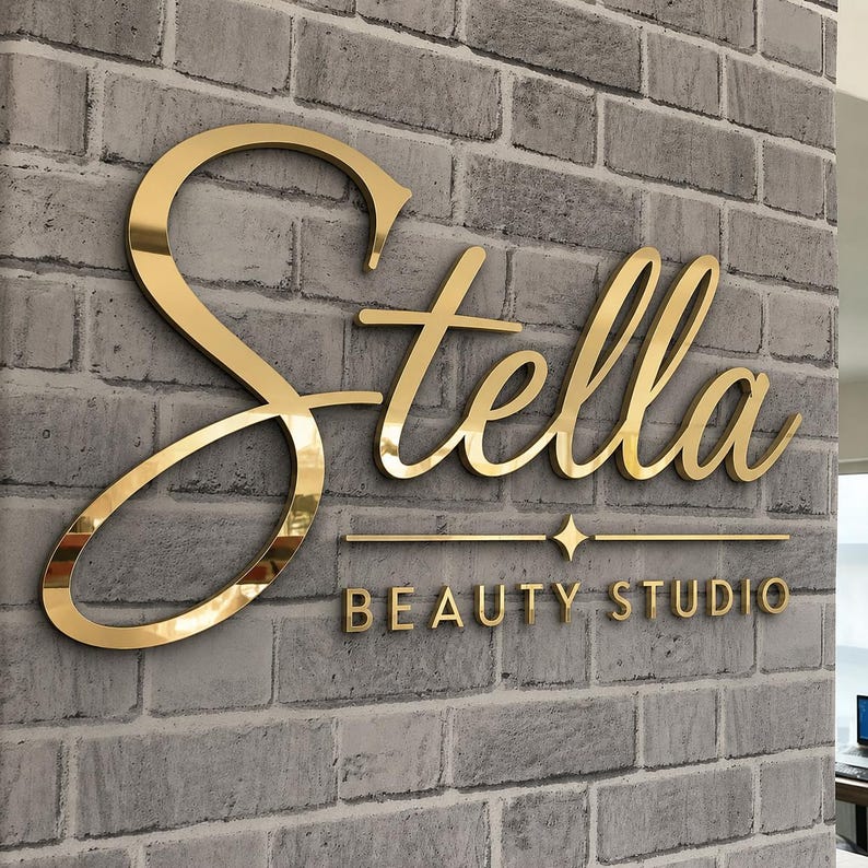 May include: A three-dimensional wall sign featuring the word Stella in a large, gold, reflective script font, positioned above the text BEAUTY STUDIO in a smaller, gold, sans-serif font, separated by a horizontal line with a central star.