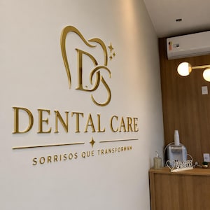 May include: A wall-mounted sign featuring gold-colored 3D lettering and a logo. The logo depicts a stylized tooth containing the letters D and S. Below the logo, the text reads DENTAL CARE, followed by the phrase SORRISOS QUE TRANSFORMAM.