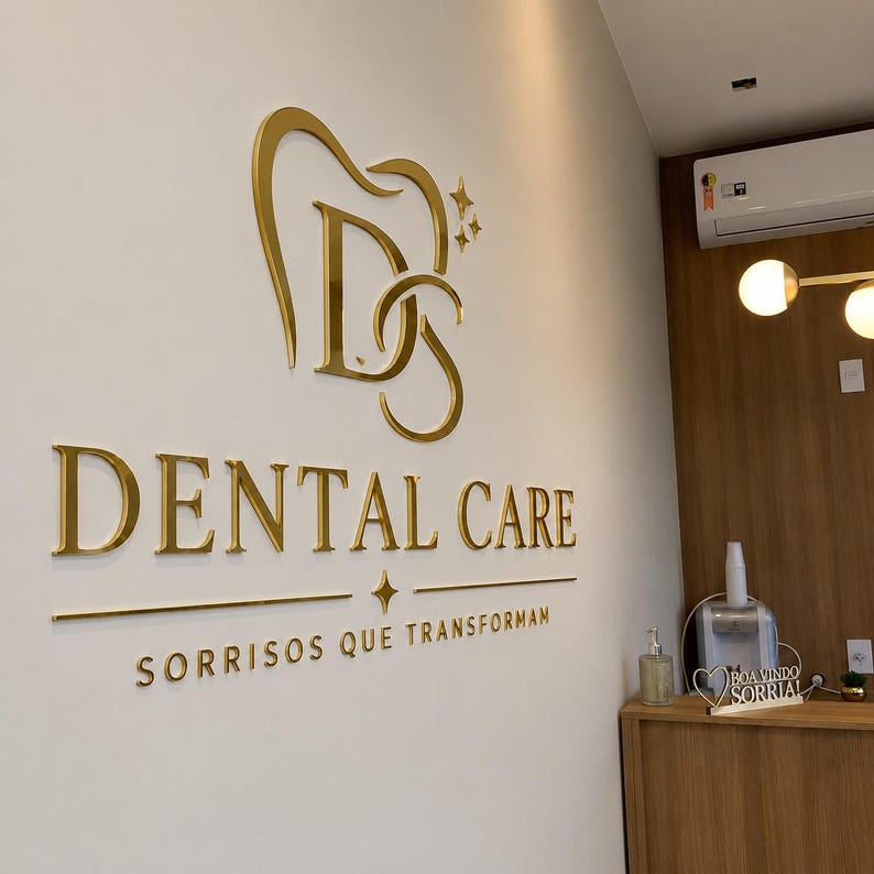 May include: A wall-mounted sign featuring gold-colored 3D lettering and a logo. The logo depicts a stylized tooth containing the letters D and S. Below the logo, the text reads DENTAL CARE, followed by the phrase SORRISOS QUE TRANSFORMAM.
