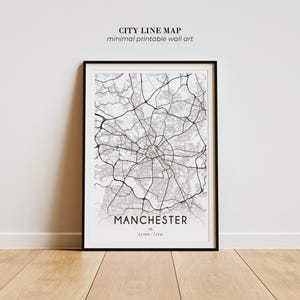 May include: A framed wall art print featuring a black and white city line map of Manchester, UK. The map displays intricate road networks in black lines against a light grey background. The text reads CITY LINE MAP, minimal printable wall art, MANCHESTER, UK, 53.48N | 2.24W.