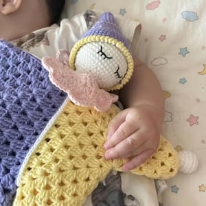 May include: A handmade crochet security blanket featuring a small doll head with a purple pointed hat, a light pink ruffled collar, and a yellow textured blanket body. The doll has embroidered closed eyes and a white pom-pom on the corner.