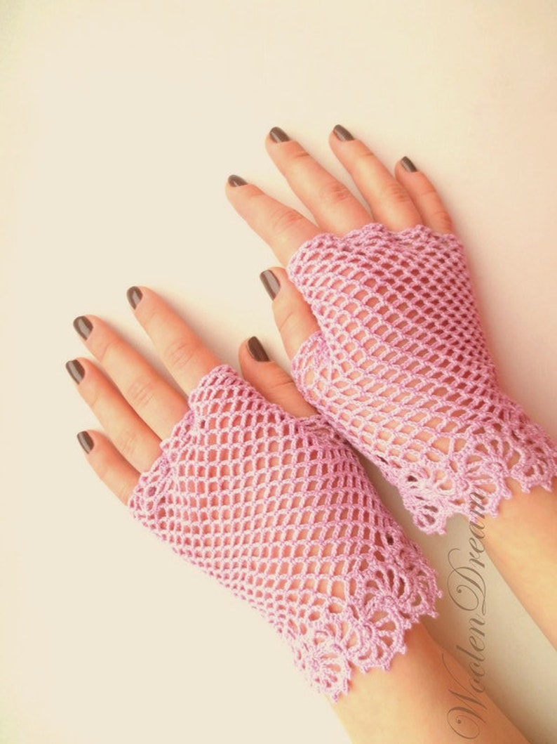 May include: A pair of pink crocheted fingerless gloves with a delicate lace trim. The gloves are made with a mesh pattern and have a light pink color.