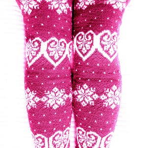 May include: Burgundy knee-high leg warmers with white snowflake and heart patterns. The knitted leg warmers have a ribbed cuff and are adorned with the text "WoolenDream". These warmers are perfect for winter wear.