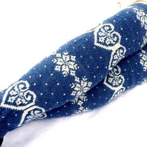 May include: A pair of blue knitted leg warmers with a white snowflake and heart design. The leg warmers are made of a soft, textured material and are designed to keep legs warm. The leg warmers are a winter accessory.