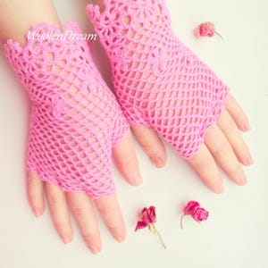 May include: A pair of pink crocheted fingerless gloves with a delicate lace pattern. The gloves are made with a fine yarn and have a loose, airy feel.