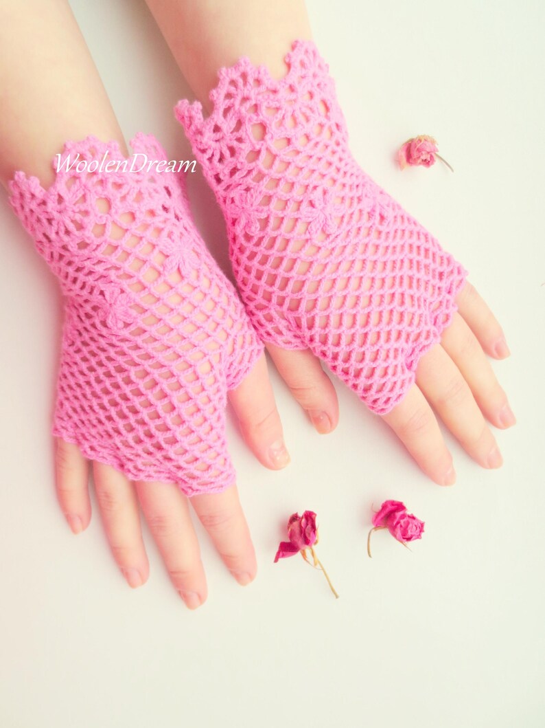 May include: A pair of pink crocheted fingerless gloves with a delicate lace pattern. The gloves are made with a fine yarn and have a loose, airy feel.