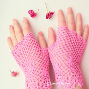 May include: A pair of pink crocheted fingerless gloves with a delicate lace trim. The gloves are made with a fine, open-weave pattern.