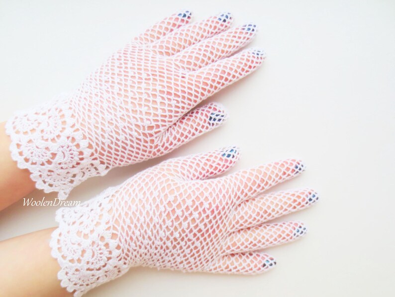 May include: A pair of white lace gloves with a delicate floral pattern at the wrist. The gloves are made of a fine mesh fabric.