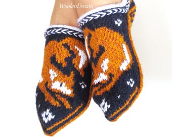 May include: A pair of knitted slippers with a fox design. The slippers are primarily orange and navy blue, with white accents. The top edge has a white and navy blue braided trim. The text "WoolenDream" is visible.