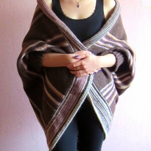 May include: A brown and white striped knitted cardigan with a long, flowing design. The cardigan is worn over a black vest top and black trousers.