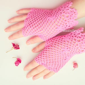 May include: A pair of pink crocheted fingerless gloves with a delicate lace pattern. The gloves are made with a fine yarn and have a lightweight, airy feel.