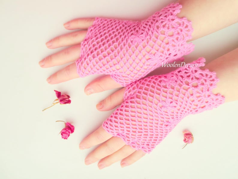 May include: A pair of pink crocheted fingerless gloves with a delicate lace pattern. The gloves are made with a fine yarn and have a lightweight, airy feel.