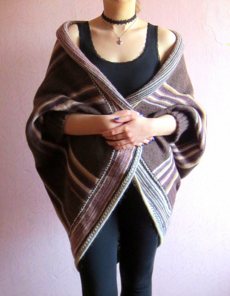 May include: A brown and white striped knitted cardigan with a long, flowing design. The cardigan is worn over a black vest top and black trousers.