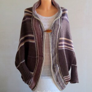 May include: A brown, white and pink striped knitted cardigan with a shawl collar and a wooden button closure. The cardigan has a relaxed fit and long sleeves.