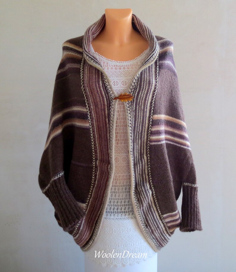 May include: A brown, white and pink striped knitted cardigan with a shawl collar and a wooden button closure. The cardigan has a relaxed fit and long sleeves.