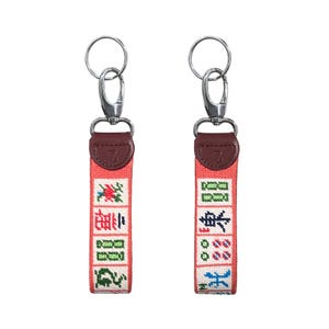 May include: Two keychains with red fabric straps featuring embroidered Chinese characters and designs. Each keychain has a silver-colored clasp and a brown leather accent with a letter "Z".