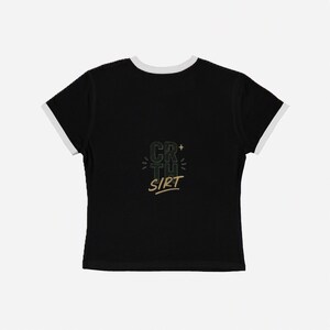 Peut inclure: Un t-shirt noir à bordures contrastées avec une finition blanche sur le col et les manches. Le centre de la poitrine présente un motif graphique avec le texte CR TH SIRT disposé en colonne, agrémenté de petites lignes et d'une étoile dorée.