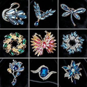 Può includere: Una collezione di nove spille decorative con vari design, tra cui un cigno, una libellula, una farfalla e motivi floreali. Ogni pezzo è realizzato con montature in metallo e intarsiato con cristalli sfaccettati blu, verdi, rosa e trasparenti.
