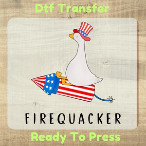 May include: A DTF transfer featuring a white goose wearing a red, white, and blue striped top hat, riding a red, white, and blue firework rocket. The text reads Dtf Transfer, FIREQUACKER, and Ready To Press in black and light green lettering.