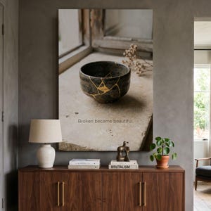 May include: A wall art print featuring a dark gray ceramic bowl repaired with gold lacquer in the kintsugi style, resting on a stone surface. The text "Broken became beautiful." is printed below the bowl in a simple, clean sans-serif font.