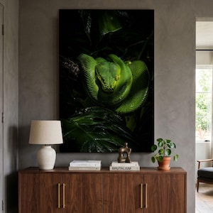 May include: A large rectangular wall art print featuring a vibrant green emerald tree boa coiled tightly on a dark branch amidst deep green tropical foliage. The snake has prominent yellow eyes and textured scales, set against a dark background.