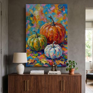 May include: An oil painting on canvas featuring three pumpkins in shades of orange, green, and white. The artwork uses thick, textured brushstrokes with a vibrant, multi-coloured background of autumn leaves in blue, yellow, pink, and red hues.