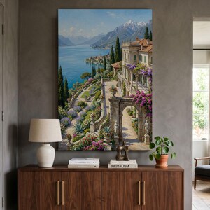 May include: A vertical wall art print depicting a Mediterranean villa terrace overlooking a blue lake and snow-capped mountains. The scene features stone arches, blooming purple bougainvillea, manicured gardens, and classical statues along a pathway.