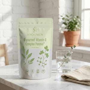May include: A white and light green pouch of "HYOOMEN B yourself Vitamin B Complex Panmol" with leaf illustrations. A glass of water with a sprig of greenery and a beige cloth are next to the pouch. The pouch contains 30 daily doses.