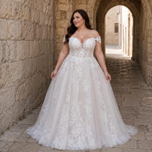 May include: An off-the-shoulder wedding dress featuring a sweetheart neckline and a fitted bodice with intricate white floral lace appliqués. The full-length skirt is crafted from layers of tulle, showcasing a cascading lace pattern that extends down.