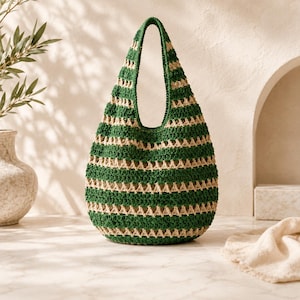 May include: A crochet hobo bag featuring alternating horizontal stripes of forest green and beige yarn. The bag has a single integrated shoulder strap and a rounded, slouchy silhouette with an open-work stitch pattern throughout the body.