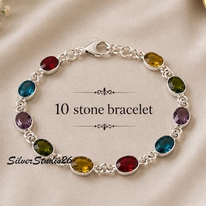 Pode incluir: Uma pulseira de corrente prateada com dez pedras preciosas de corte oval em tons de vermelho, azul, verde e roxo. A pulseira inclui um fecho lagosta e apresenta o texto 10 stone bracelet e SilverStudio26 no centro da imagem.