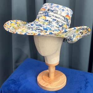 May include: A quilted sun hat featuring a vibrant pattern of yellow lemons and blue floral motifs on a white background. The hat has a wide, flexible brim and a structured crown, showcasing detailed stitching throughout the fabric construction.