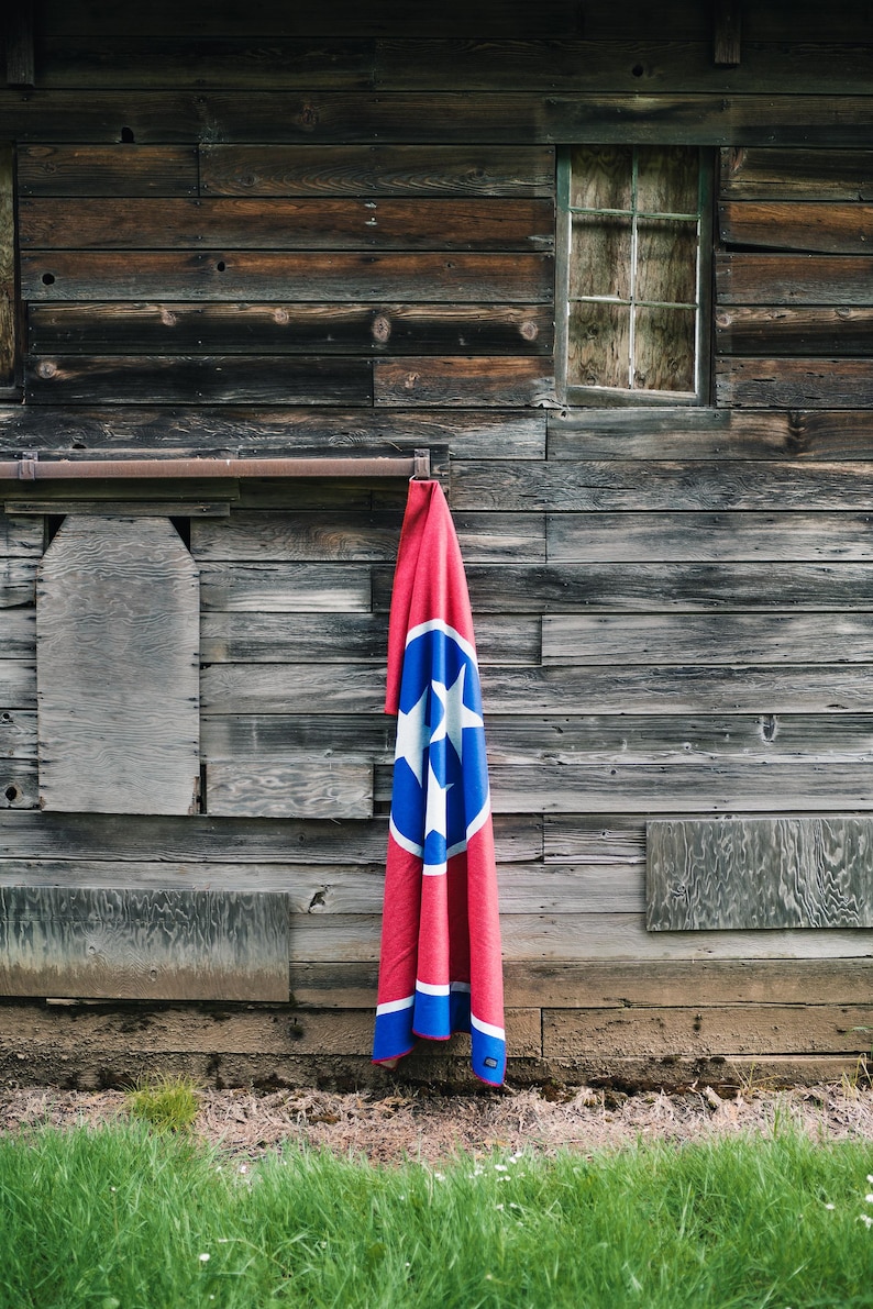 May include: A red and blue blanket with the Tennessee state flag design hanging on a weathered wooden wall. The blanket features a large blue circle with three white stars and a white border.