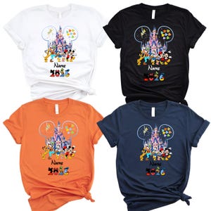 K&ouml;nnte beinhalten: Vier kurz&auml;rmelige T-Shirts in Wei&szlig;, Schwarz, Orange und Marineblau. Jedes zeigt eine Schlossgrafik in einer Micky-Maus-Ohren-Silhouette, mit Zeichentrickfiguren, dem Wort Name und der Jahreszahl 2026 in bunten, gemusterten Buchstaben.