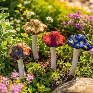 May include: Four ceramic mushroom garden stakes with white stems and glossy, multi-colored caps. The caps feature distinct glaze patterns in shades of brown, red, blue, and a multi-colored blend, each supported by a slender, solid white cylindrical base.