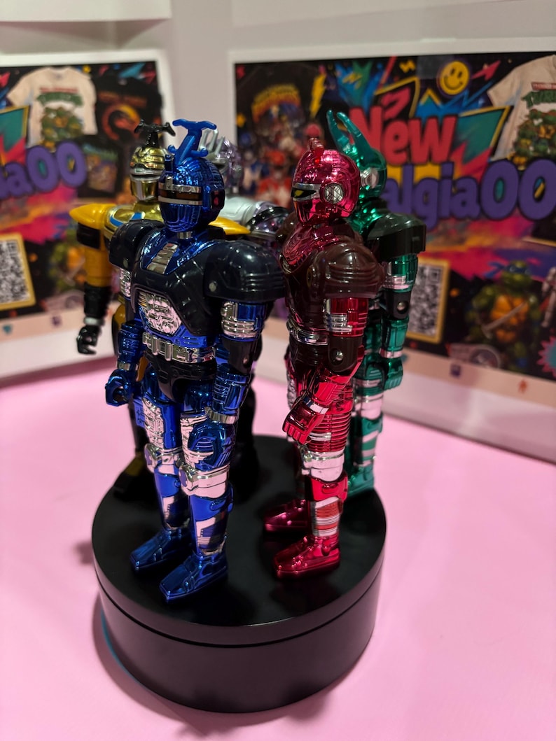 May include: A group of four metallic action figures standing on a black circular rotating display base. The figures feature shiny blue, red, green, and yellow finishes with insect-like helmet designs and detailed armor plating on their bodies.
