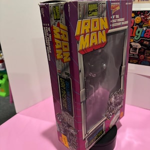 May include: A boxed Iron Man action figure from Marvel Comics. The box is purple and silver with the Iron Man logo and the words "Deluxe Edition War Machine." The figure is 10 inches tall and fully poseable.