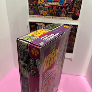 May include: A vintage Iron Man action figure box. The box is purple and features the Iron Man logo in yellow and red. The box also includes the text "10" tall, fully poseable, and accessory included."