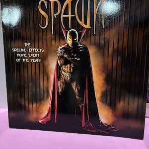 May include: A square DVD case for the film Spawn Director's Cut. The cover features the character Spawn in a dark suit with a long red cape, standing against a vertical barred background. Text reads: Director's Cut, Spawn, The Special-Effects Movie Event Of The Year!