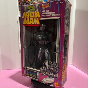 May include: Deluxe Edition War Machine Iron Man action figure in its original packaging. The box is pink and purple with the Marvel Comics logo and the text "10" tall, fully poseable, accessory included". The figure is visible through a clear plastic window.