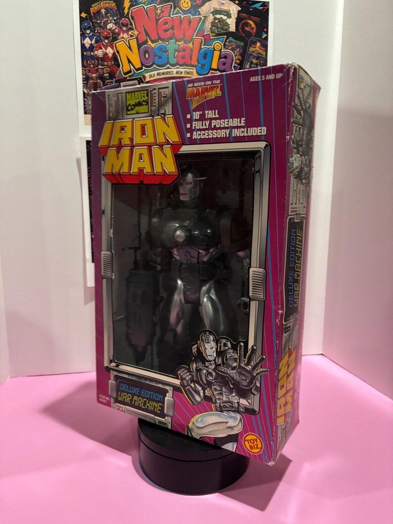 May include: Deluxe Edition War Machine Iron Man action figure in its original packaging. The box is pink and purple with the Marvel Comics logo and the text "10" tall, fully poseable, accessory included". The figure is visible through a clear plastic window.