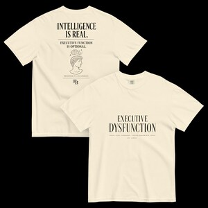 Op de afbeelding: Een crèmekleurig t-shirt met korte mouwen en zwarte tekst en afbeeldingen. De voorkant toont "EXECUTIVE DYSFUNCTION" met "HIGH STANDARDS, LIMITED BANDWIDTH" eronder. De achterkant toont "INTELLIGENCE IS REAL." en "EXECUTIVE FUNCTION IS OPTIONAL." boven een lijntekening van een buste met een brein en de tekst "DESIGNED IN LOS ANGELES" en "HB".