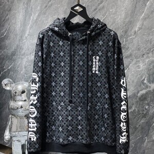 May include: Black hoodie with a repeating cross pattern and white text on the sleeves and chest. The hoodie has a drawstring hood and a front pocket. The garment is hanging on a gold-colored rod.