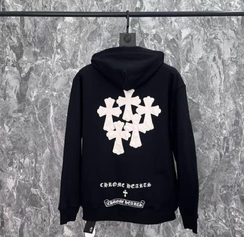K&ouml;nnte beinhalten: Schwarzer Kapuzenpullover mit wei&szlig;em Kreuzmuster auf dem R&uuml;cken. Der Text "CHROME hearts" ist unter dem Kreuzmuster aufgedruckt. Der Pullover hat eine Kapuze mit Kordelzug und eine K&auml;ngurutasche.