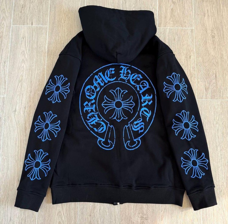 Puede incluir: Sudadera con capucha negra con cremallera, capucha y dise&ntilde;os gr&aacute;ficos azules. La parte trasera presenta un gran dise&ntilde;o circular con las palabras "Chrome Hearts" y una cruz. Las mangas tienen m&uacute;ltiples dise&ntilde;os en forma de cruz.