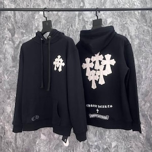 K&ouml;nnte beinhalten: Zwei schwarze Kapuzenpullover mit wei&szlig;en Kreuzmustern. Einer hat ein einzelnes Kreuz auf der Vorderseite, der andere mehrere Kreuze auf der R&uuml;ckseite. Beide haben den Markennamen und das Logo aufgedruckt.