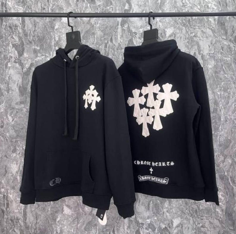 K&ouml;nnte beinhalten: Zwei schwarze Kapuzenpullover mit wei&szlig;en Kreuzmustern. Einer hat ein einzelnes Kreuz auf der Vorderseite, der andere mehrere Kreuze auf der R&uuml;ckseite. Beide haben den Markennamen und das Logo aufgedruckt.