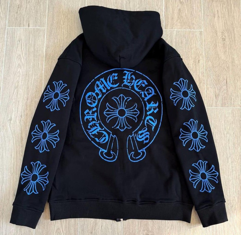 Puede incluir: Sudadera con capucha negra con cremallera y dise&ntilde;os gr&aacute;ficos azules. La parte trasera presenta un gran dise&ntilde;o circular con el texto "Chrome Hearts" y un emblema de cruz. Las mangas tienen m&uacute;ltiples dise&ntilde;os florales azules en forma de cruz.