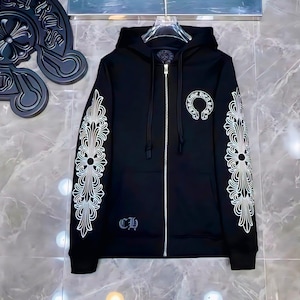 May include: A black zip-up hoodie featuring white graphic prints on both sleeves and the left chest. The design includes ornate floral-like patterns on the sleeves and a circular logo on the chest. A small CH logo is printed near the bottom hem.