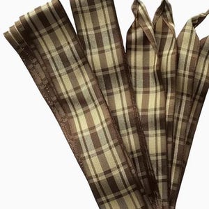 May include: A set of flat shoelaces featuring a brown and cream plaid pattern. The laces are constructed from a woven fabric material and include clear plastic aglets at the tips to prevent fraying and facilitate easy threading through eyelets.